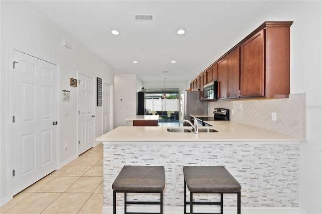 kitchen featuring light tile patterned flooring, a sink, a peninsula, decorative backsplash, and appliances with stainless steel finishes