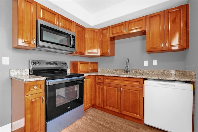 kitchen with light wood-style flooring, appliances with stainless steel finishes, light stone counters, a sink, and brown cabinets
