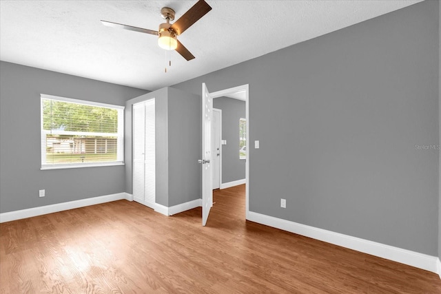 unfurnished room with a textured ceiling, wood finished floors, ceiling fan, and baseboards