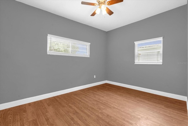 spare room with baseboards, ceiling fan, wood finished floors, and a healthy amount of sunlight
