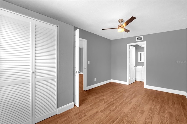 unfurnished bedroom featuring visible vents, a closet, ensuite bathroom, baseboards, and light wood-style flooring