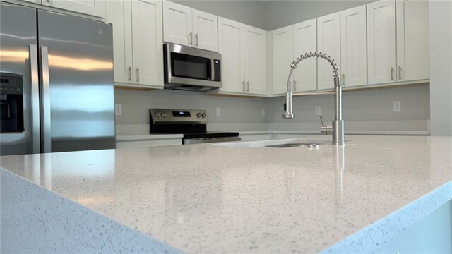 16435 SW 27th Ave, Ocala, FL 34473 - kitchen featuring appliances with stainless steel finishes, a sink, light stone countertops, and white cabinetry