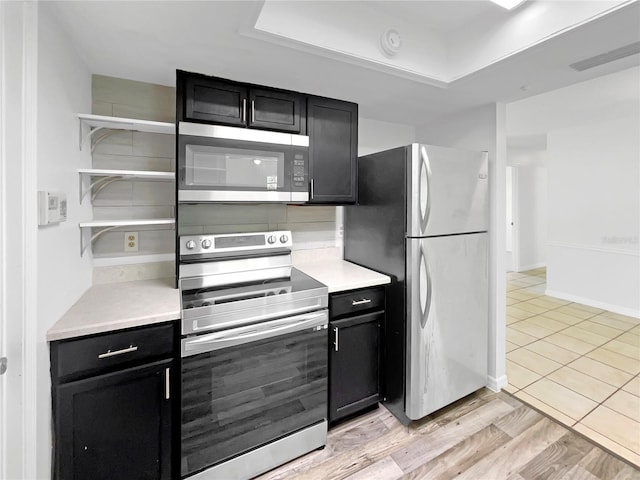 kitchen with dark cabinetry, light countertops, open shelves, and stainless steel appliances