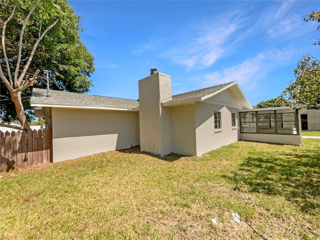 back of property with a sunroom, a chimney, fence, and a lawn