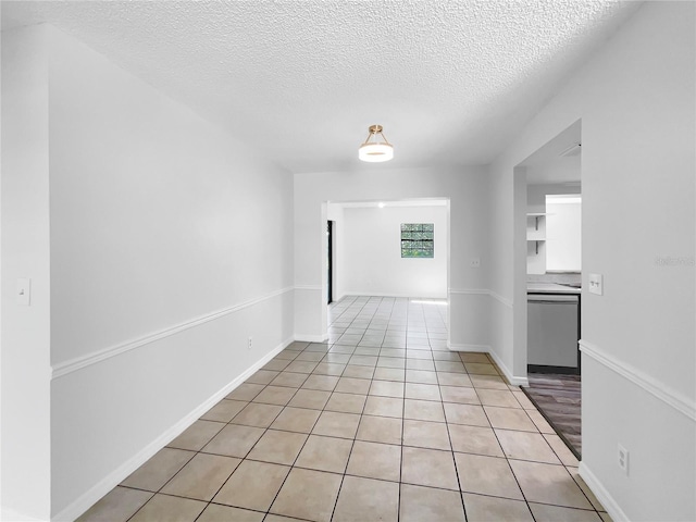 spare room featuring a textured ceiling, light tile patterned flooring, and baseboards
