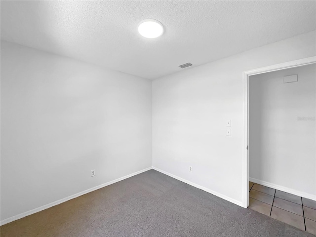 carpeted empty room featuring visible vents, a textured ceiling, and baseboards