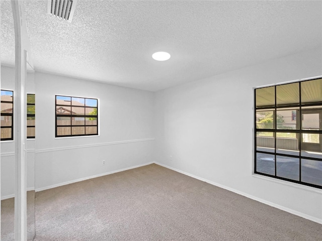 carpeted spare room with visible vents, baseboards, and a textured ceiling