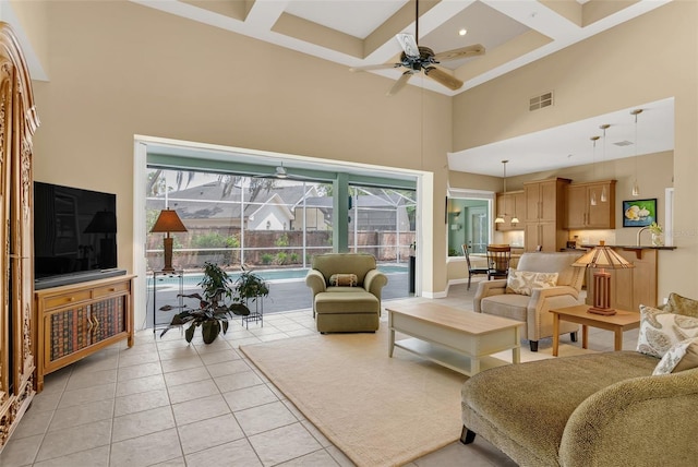 living area featuring a healthy amount of sunlight, coffered ceiling, visible vents, a ceiling fan, and a high ceiling