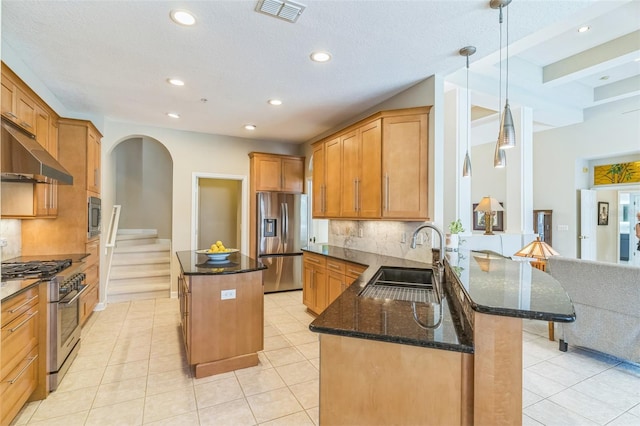 kitchen featuring stainless steel appliances, under cabinet range hood, a center island, a sink, and visible vents