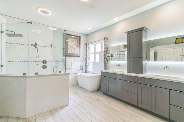 bathroom featuring a shower stall, a sink, double vanity, a freestanding tub, and wood finished floors