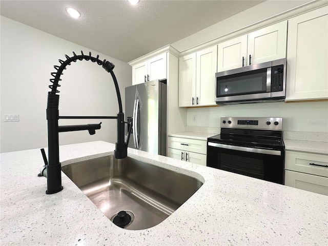 kitchen with white cabinets, appliances with stainless steel finishes, light stone counters, a sink, and a textured ceiling