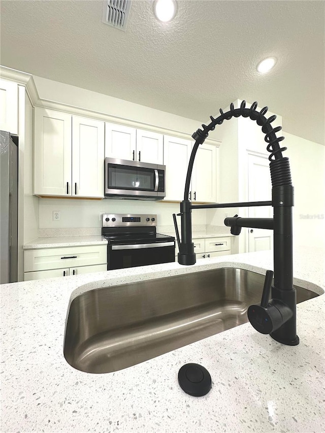 details featuring visible vents, light stone countertops, a textured ceiling, white cabinetry, and stainless steel appliances