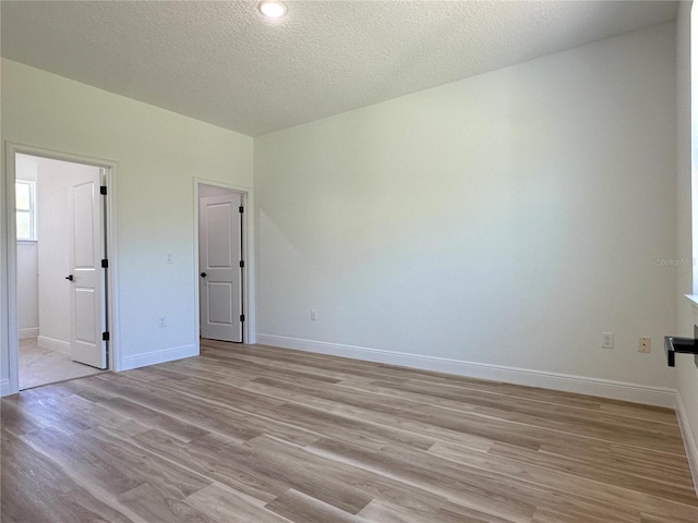 unfurnished bedroom featuring baseboards, light wood-type flooring, a textured ceiling, and connected bathroom