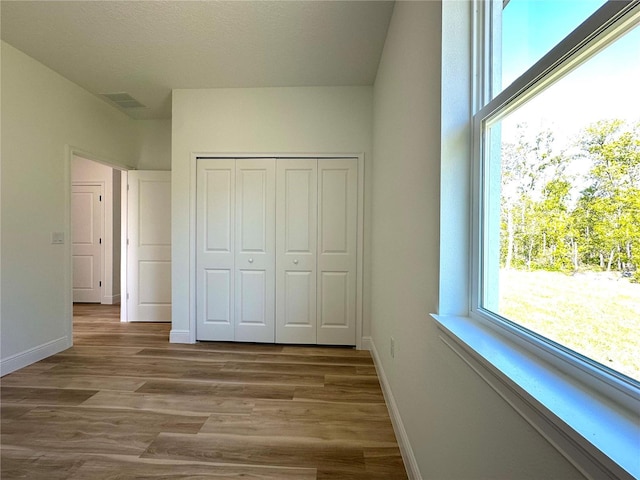 unfurnished bedroom with a closet, baseboards, wood finished floors, and visible vents
