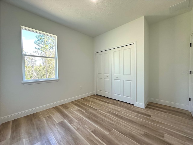 unfurnished bedroom featuring a textured ceiling, baseboards, multiple windows, and light wood-type flooring