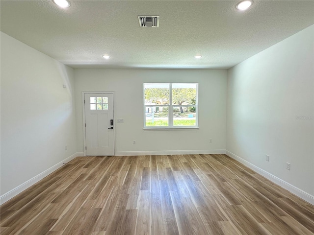 foyer featuring visible vents, a textured ceiling, baseboards, and wood finished floors
