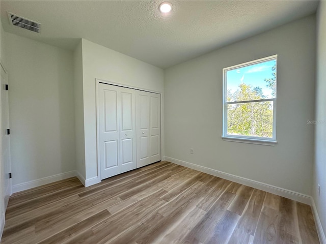 unfurnished bedroom featuring a textured ceiling, baseboards, wood finished floors, visible vents, and a closet