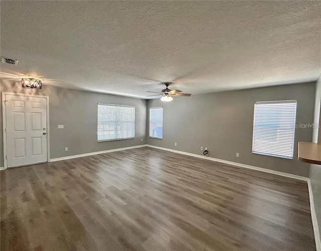 unfurnished living room featuring a healthy amount of sunlight, visible vents, a ceiling fan, and wood finished floors