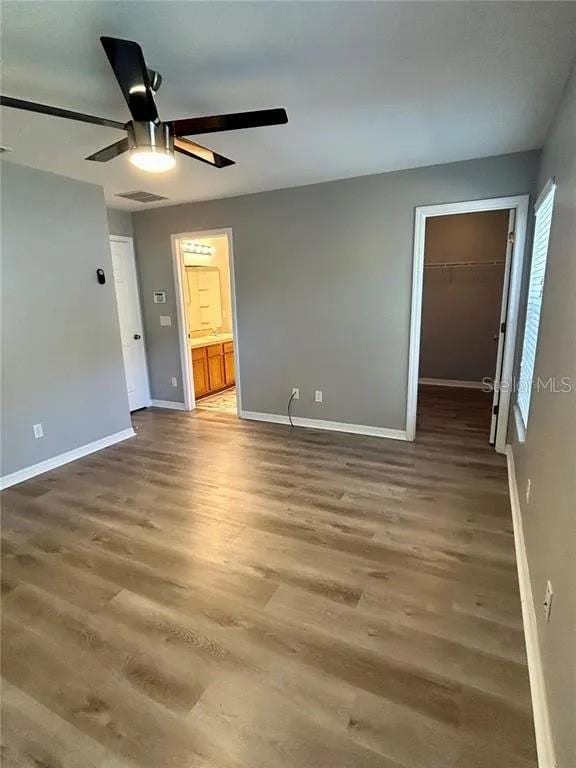 unfurnished bedroom with a walk in closet, wood finished floors, baseboards, and visible vents