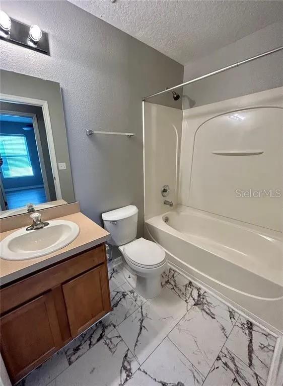 full bathroom featuring vanity, bathing tub / shower combination, a textured ceiling, toilet, and marble finish floor