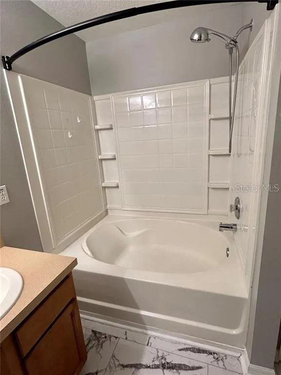 bathroom with marble finish floor, vanity, bathtub / shower combination, and a textured ceiling