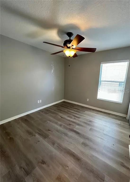 spare room featuring a textured ceiling, wood finished floors, baseboards, and a ceiling fan