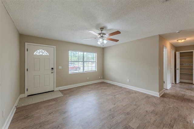 entryway with a textured ceiling, wood finished floors, ceiling fan, and baseboards