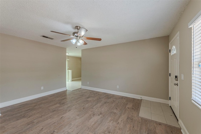 empty room featuring visible vents, baseboards, a ceiling fan, a textured ceiling, and wood finished floors