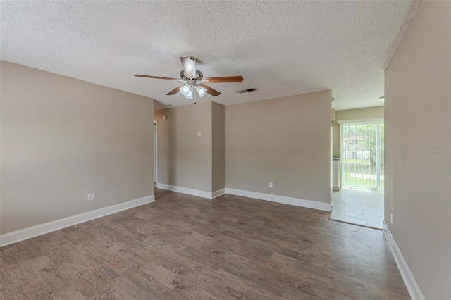 empty room with a textured ceiling, wood finished floors, a ceiling fan, and visible vents