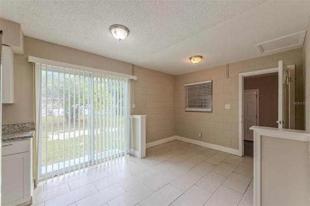 unfurnished room with a textured ceiling, attic access, and light tile patterned floors