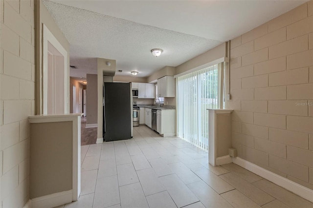 kitchen featuring a textured ceiling, appliances with stainless steel finishes, light tile patterned flooring, and white cabinets