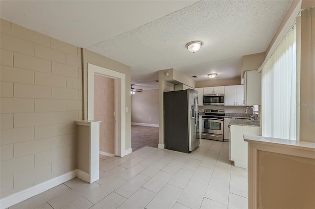 kitchen with appliances with stainless steel finishes, light stone counters, white cabinetry, ceiling fan, and a sink