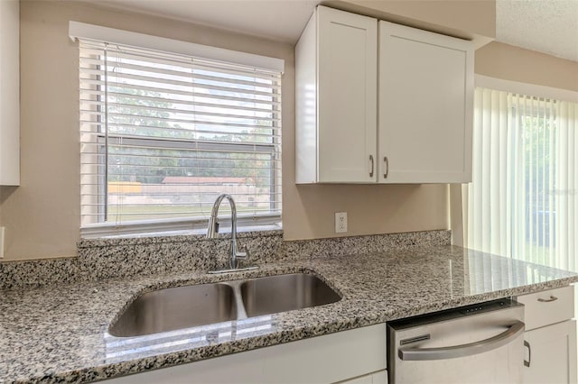 kitchen with stainless steel dishwasher, a sink, and white cabinetry
