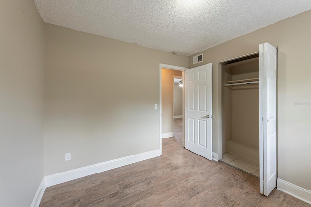 unfurnished bedroom with a textured ceiling, a closet, visible vents, wood finished floors, and baseboards