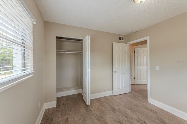 unfurnished bedroom featuring light wood-type flooring, a closet, a textured ceiling, visible vents, and baseboards