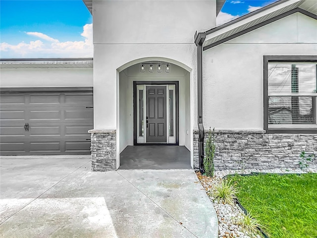view of exterior entry with concrete driveway, a garage, stucco siding, and stone siding