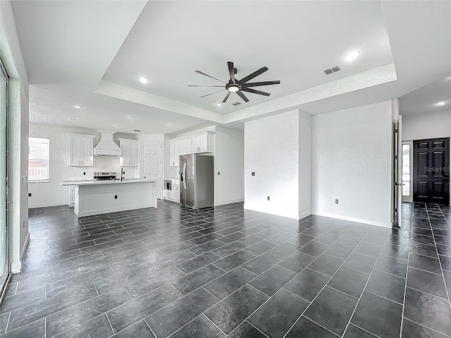 unfurnished living room with visible vents, baseboards, a raised ceiling, dark tile patterned floors, and ceiling fan