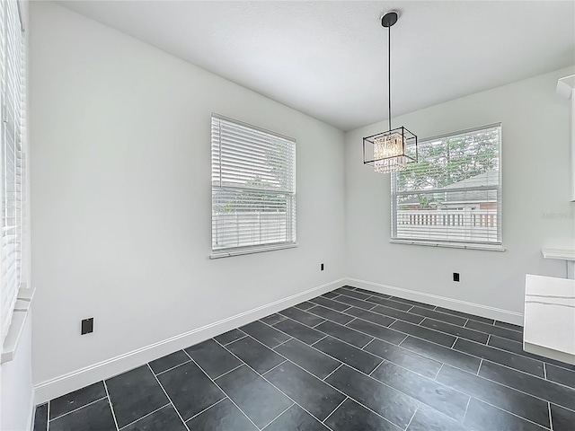 unfurnished room featuring baseboards, dark tile patterned floors, and a chandelier