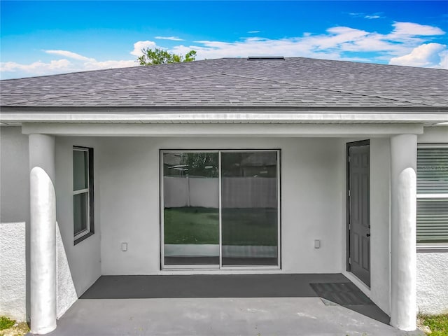 entrance to property with stucco siding and roof with shingles