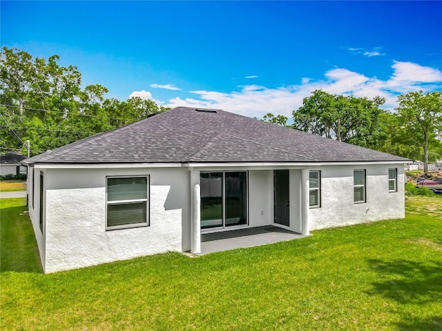 rear view of property with roof with shingles, a lawn, and stucco siding