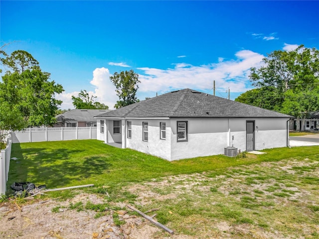 back of house featuring central AC, a lawn, fence, stucco siding, and roof with shingles