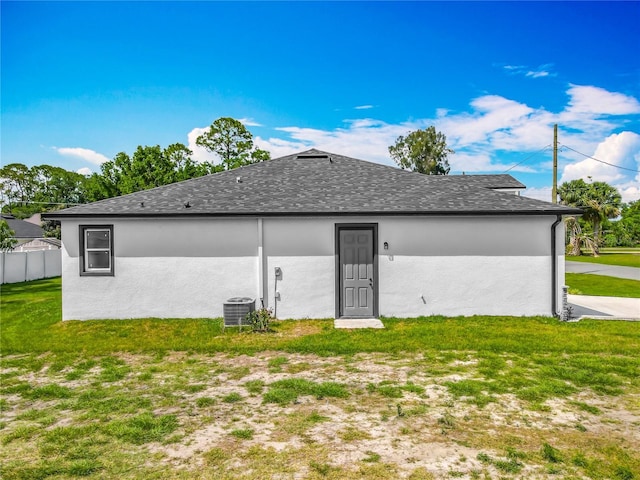 back of property featuring central AC unit, fence, a lawn, and stucco siding