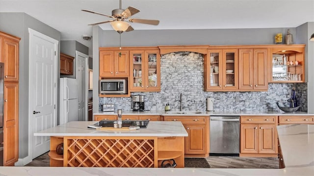 kitchen featuring light wood-style floors, tasteful backsplash, a ceiling fan, appliances with stainless steel finishes, and a sink