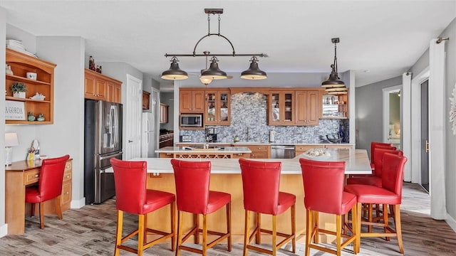 kitchen with light wood-style flooring, light countertops, an island with sink, and stainless steel appliances
