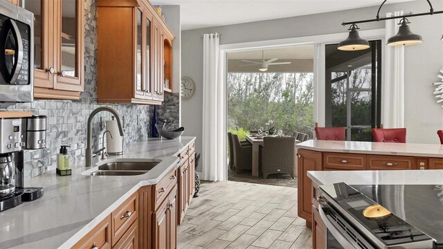 kitchen with brown cabinetry, a ceiling fan, appliances with stainless steel finishes, a sink, and backsplash