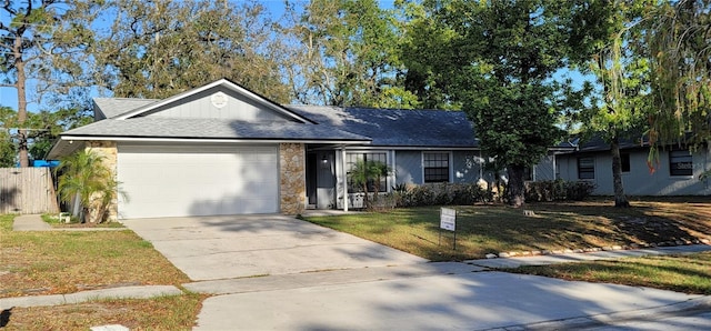 ranch-style house featuring a shingled roof, driveway, stone siding, a front lawn, and an attached garage