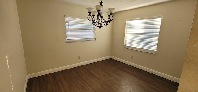 unfurnished room with baseboards, a notable chandelier, a textured ceiling, and dark wood-style flooring