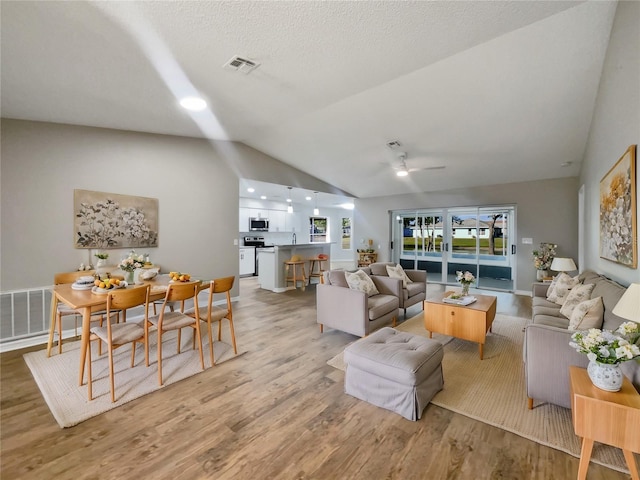 living room with ceiling fan, light wood-style flooring, a textured ceiling, visible vents, and lofted ceiling