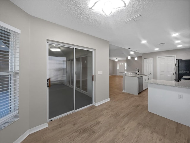 kitchen featuring a textured ceiling, decorative light fixtures, stainless steel appliances, light wood finished floors, and a sink