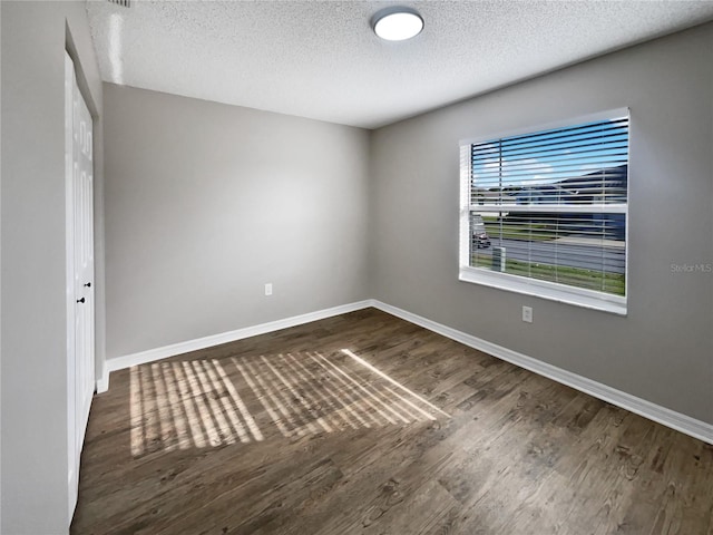 empty room featuring dark wood-type flooring, baseboards, and a textured ceiling